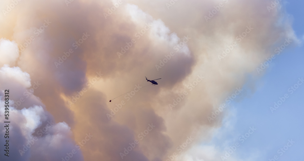 Wildfire Service Helicopter flying over BC Forest Fire and Smoke on the mountain near Hope during a hot sunny summer day. British Columbia, Canada. Natural Disaster Wildfire Service Helicopter flying over BC Forest Fire and Smoke on the mountain near Hope during a hot sunny summer day. British Columbia, Canada. Natural Disaster