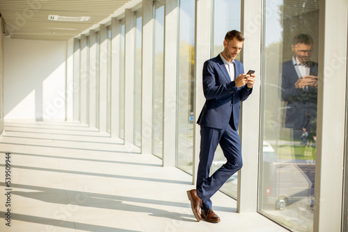 Young business man using mobile phone in the modern office hallway