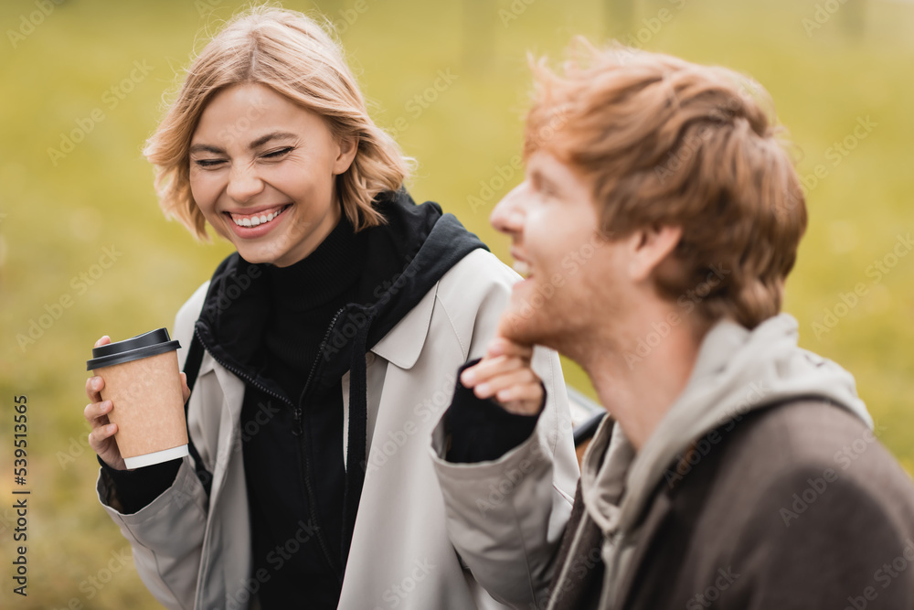 happy blonde woman holding paper cup and touching chin of redhead boyfriend. happy blonde woman holding paper cup and touching chin of redhead boyfriend.