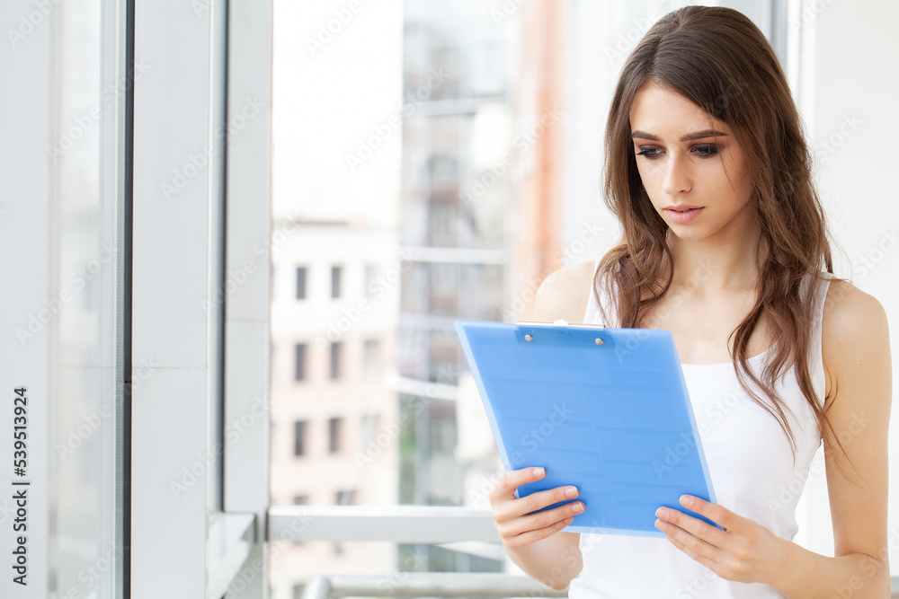 A woman in the office near the window, holding documents in her hands A woman in the office near the window, holding documents in her hands