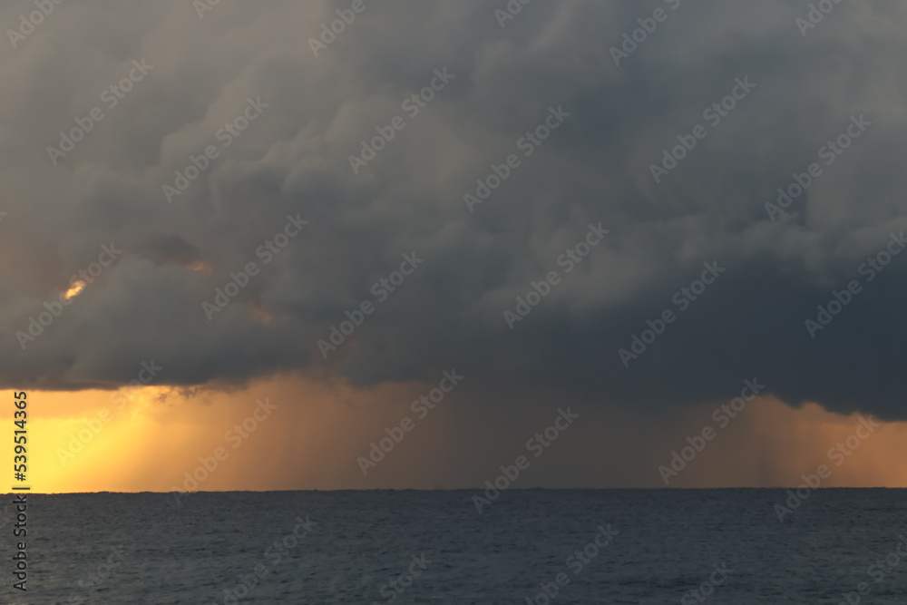 Una nube descarga con fuerza en el mar mientras sale el sol