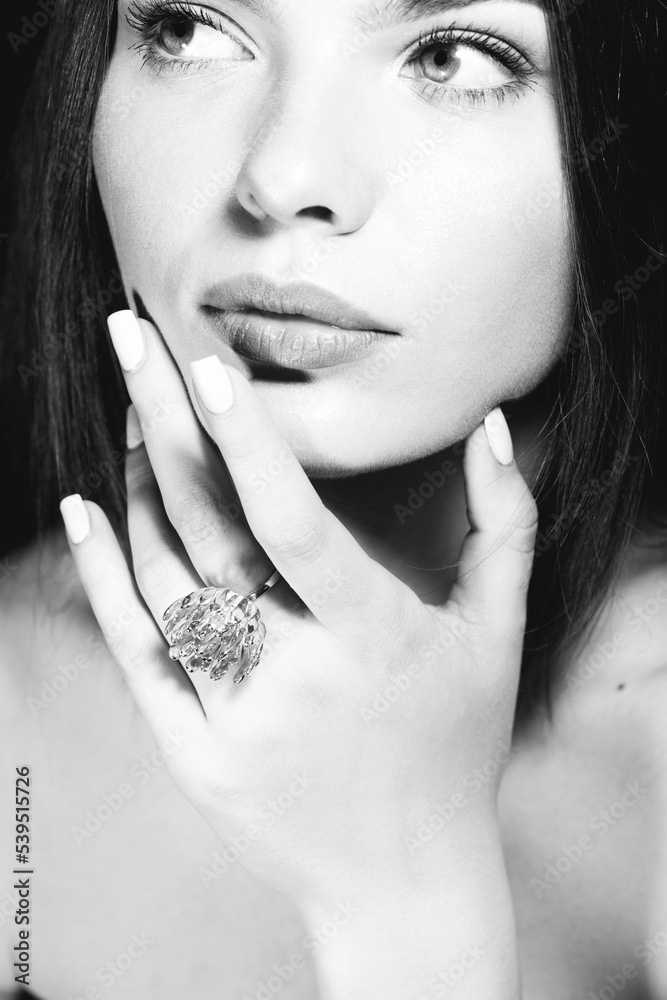 Fashion, jewelry and make-up concept. Studio portrait of beautiful and sexy woman with fancy golden ring. Model holding hand with ring near her lips and looking aside the camera. Black and white image