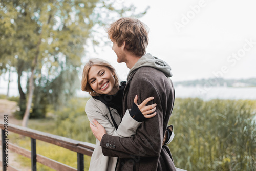 blonde woman smiling and hugging redhead man during date on bridge.