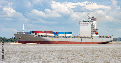 A container ship loaded with containers sails alongside the shore photo