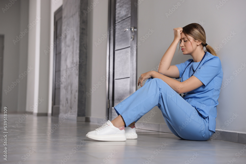 Exhausted doctor sitting on floor in hospital, space for text Exhausted doctor sitting on floor in hospital, space for text