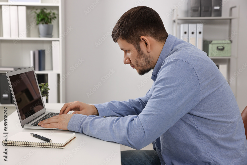 Man with poor posture working on laptop in office. Symptom of scoliosis Man with poor posture working on laptop in office. Symptom of scoliosis