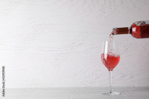 Pouring delicious rose wine into glass on table against white wooden background. Space for text