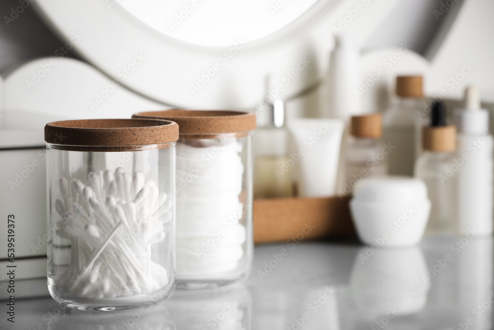 Naklejka premium Glass jars with cotton pads and swabs on dressing table. Space for text
