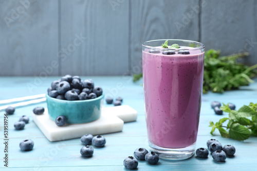 Glass of blueberry smoothie with mint and fresh berries on light blue wooden table. Space for text