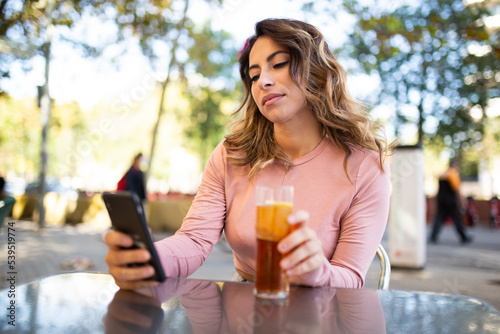 young woman sitting outdoors with mobile phone and drink