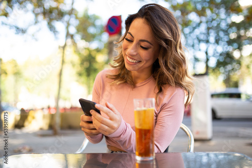 young woman sitting outside with mobile phone and drink
