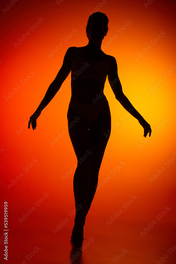 Silhouette of female full-length body isolated over orange background. Walking on tiptoe.