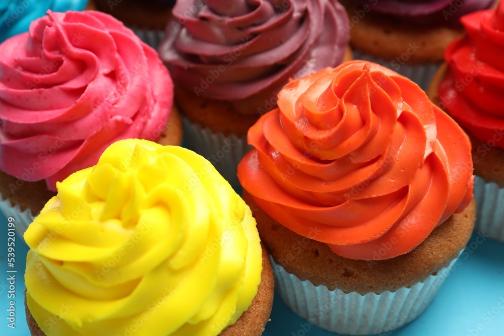 Many delicious colorful cupcakes on light blue background, closeup Many delicious colorful cupcakes on light blue background, closeup