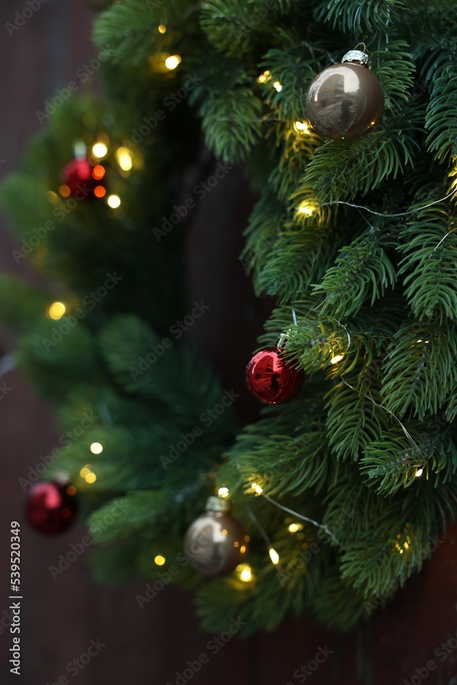 Beautiful Christmas wreath with baubles and string lights hanging on wall, closeup