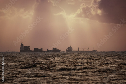 Commercial ships against dramatic cloudy sky with sunbeams