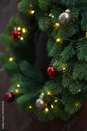 Beautiful Christmas wreath with baubles and string lights hanging on wall  closeup