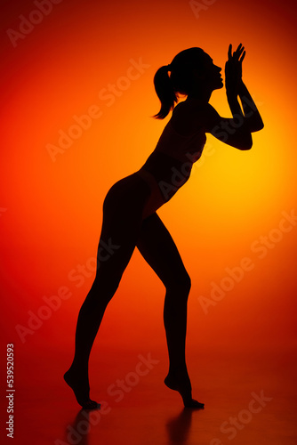 Silhouette of female full-length body isolated over orange background. tender movements