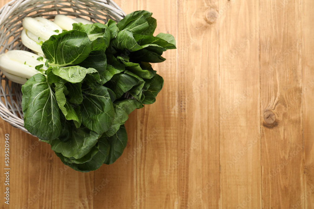 Fresh green pak choy cabbages in wicker basket on wooden table, top view. Space for text Fresh green pak choy cabbages in wicker basket on wooden table, top view. Space for text