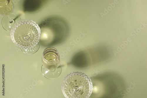 Glasses of delicious sparkling wine on light yellow background, above view. Space for text