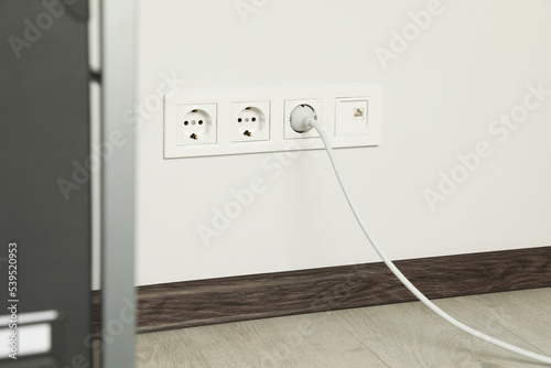 Power sockets with inserted plug on white wall indoors. Electrical supply © New Africa