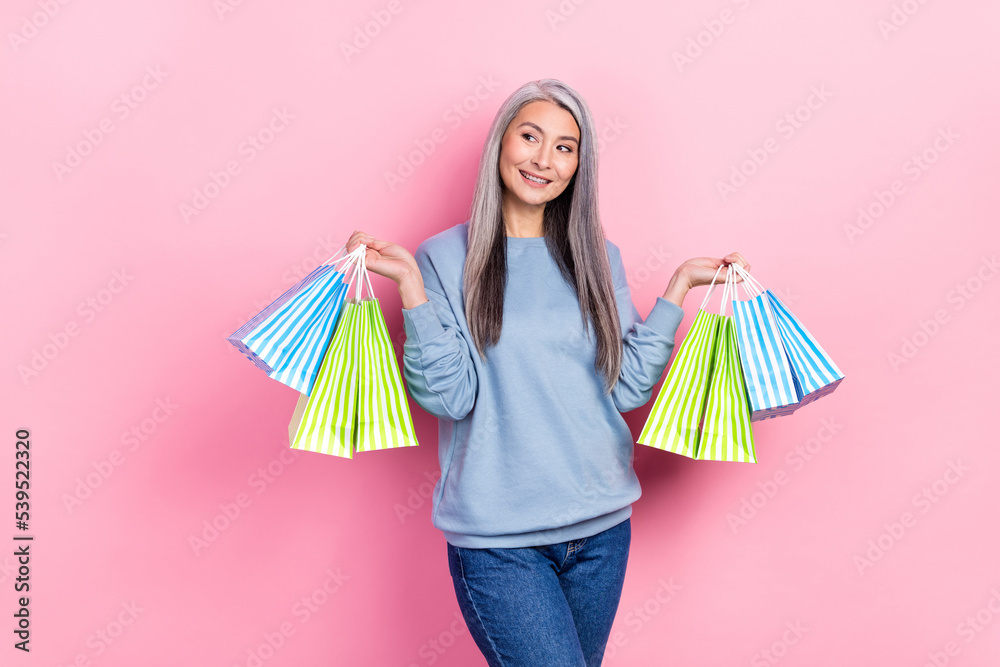 Photo of pretty dreamy lady pensioner dressed blue pullover holding begs looking empty space isolated pink color background