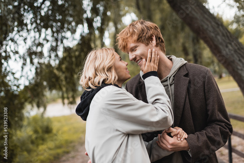 cheerful redhead man and blonde woman in coat smiling during date in park.