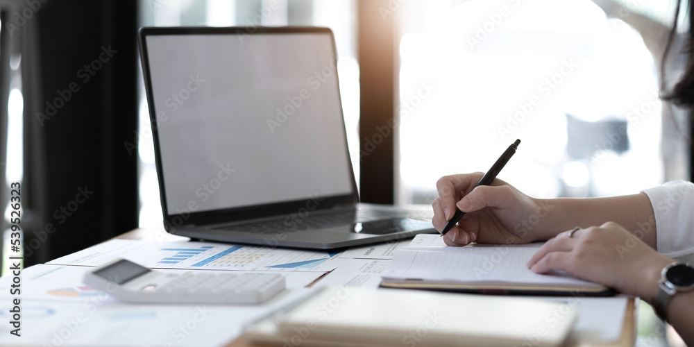 Young business woman sitting at table and taking notes in notebook.On table is laptop, smartphone Young business woman sitting at table and taking notes in notebook.On table is laptop, smartphone