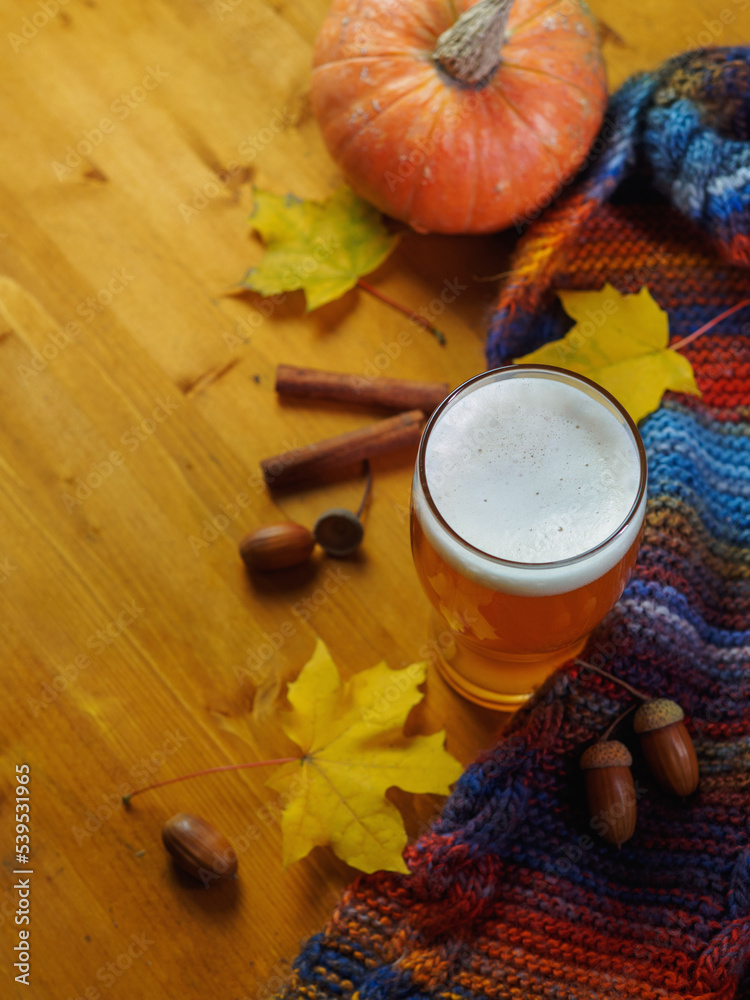 Pumpkin ale in a glass on a wooden table. Autumn decor with maple leaves, scarf, acorns and cinnamon Pumpkin ale in a glass on a wooden table. Autumn decor with maple leaves, scarf, acorns and cinnamon