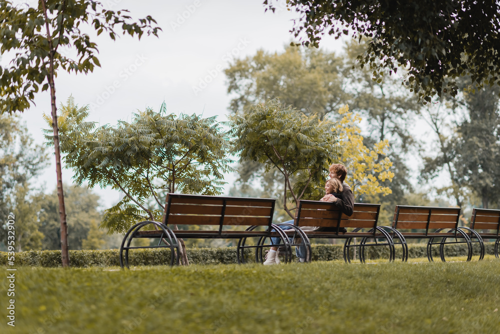 cheerful young man and woman hugging and sitting on wooden bench in green park. cheerful young man and woman hugging and sitting on wooden bench in green park.