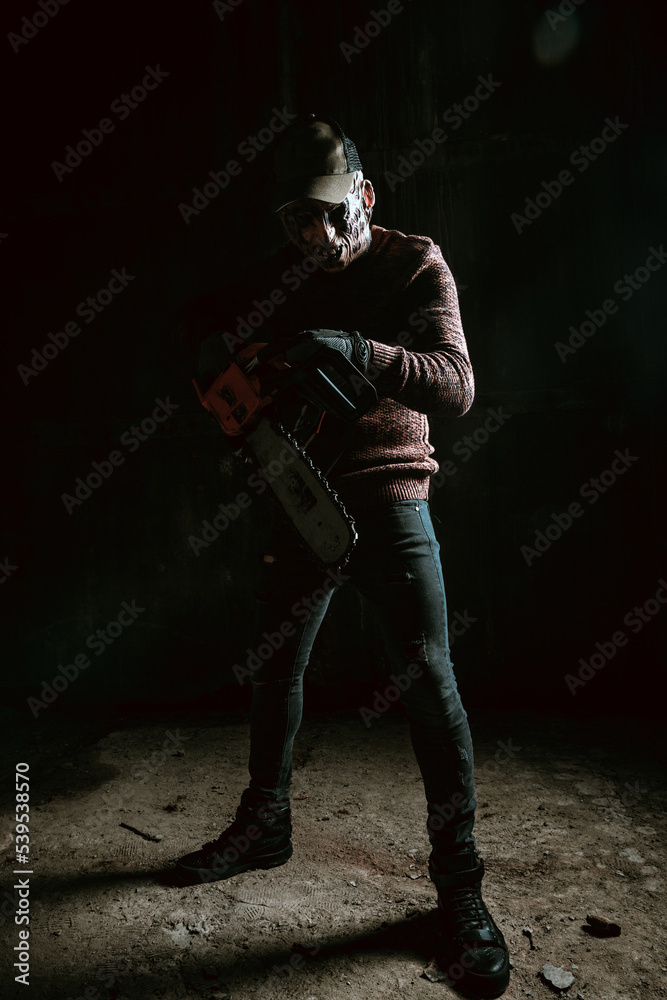 Evil in mask with chainsaw, horror Halloween scene in dark room