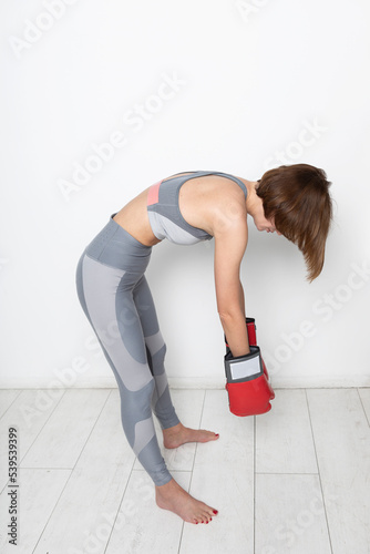 Side view on defeated female boxer in sportswear and boxing gloves standing on the floor close to the wall