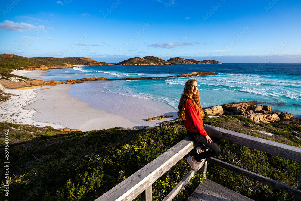 beautiful long-haired girl sits on the railing enjoying the sunset on lucky bay beach in western australia