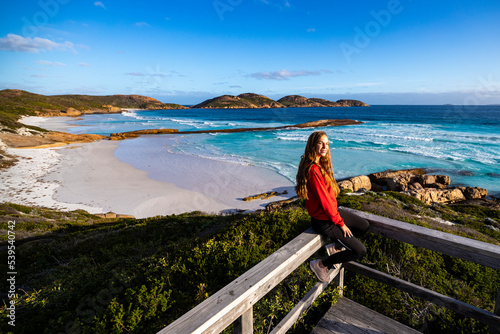 beautiful long-haired girl sits on the railing enjoying the sunset on lucky bay beach in western australia