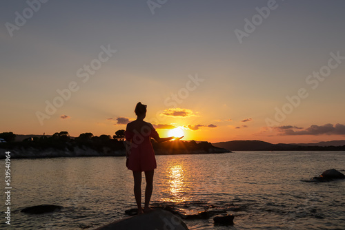 Silhouette of tourist woman holding the sun with panoramic view of sunset over Aegean Mediterranean Sea on Karydi beach, peninsula Sithonia, Chalkidiki (Halkidiki), Greece, Europe. Romantic atmosphere photo