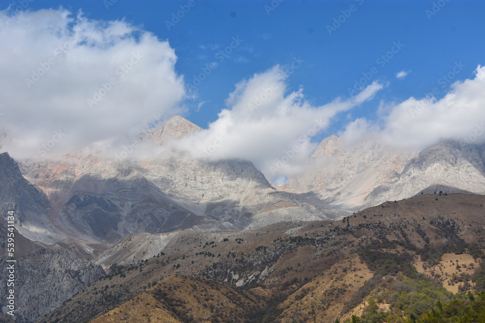 
panoramic view of the mountain range in the clouds with blue sky on the background in Arslanbob in Kyrgyzstan