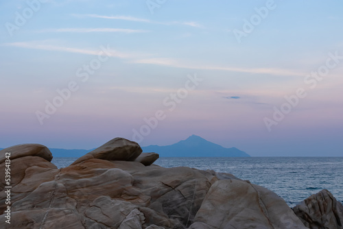 Beautiful panoramic view of holy Mount Athos at sunset seen from Karydi beach, Sithonia, Chalkidiki (Halkidiki), Greece, Europe. Summer vacation at Aegean Mediterranean Sea. Rock formations in the bay photo