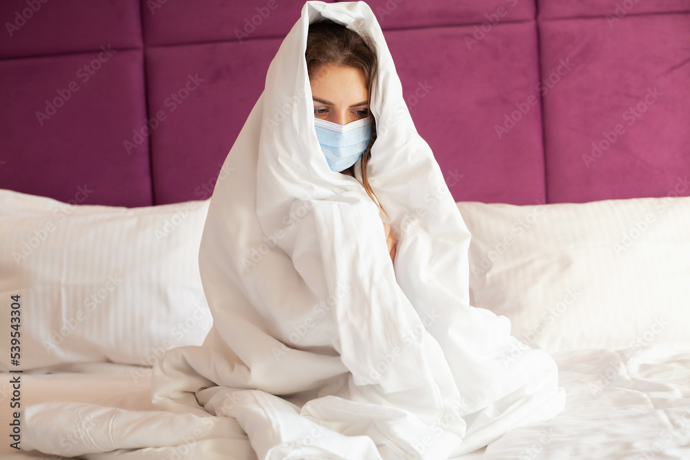 Sick woman in medical mask suffering from virus disease and fever in a bed at home Sick woman in medical mask suffering from virus disease and fever in a bed at home
