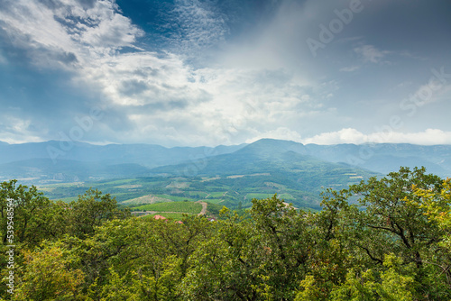 View of the hills in the distance with a cloudy stormy sky, oak trees and misty mountains in the background.