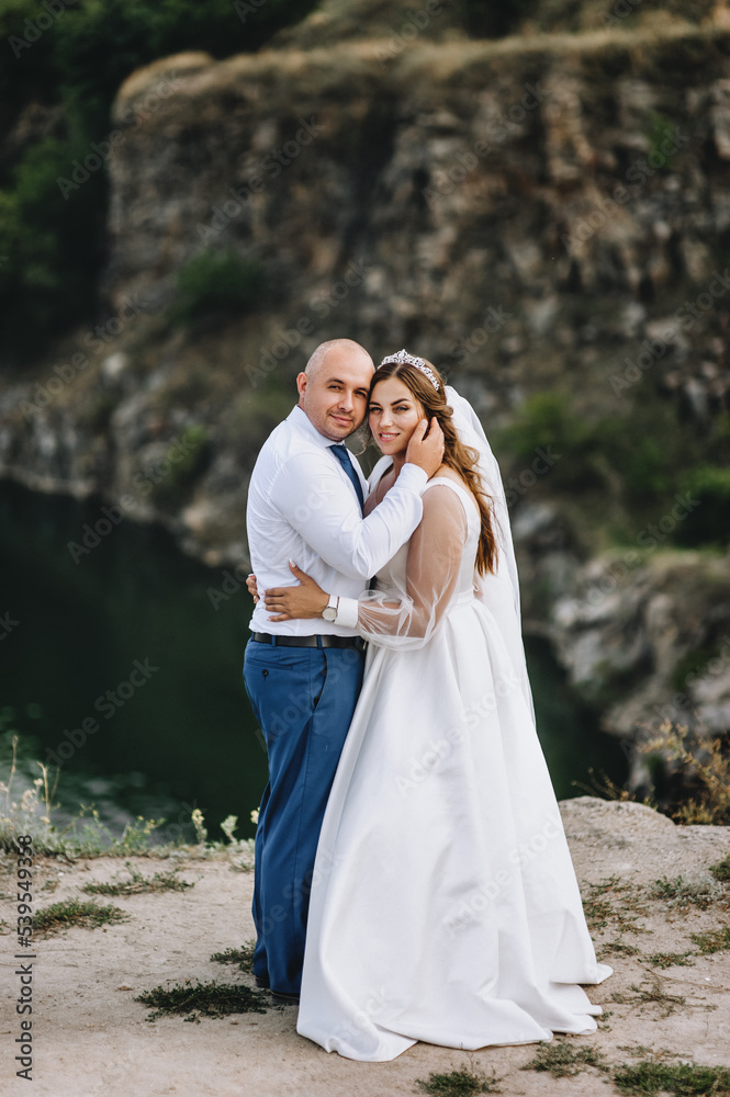 A stylish groom and a beautiful, sweet bride in a white dress are embracing in the open air, against the backdrop of rocks, mountain cliffs near the sea. wedding photography.