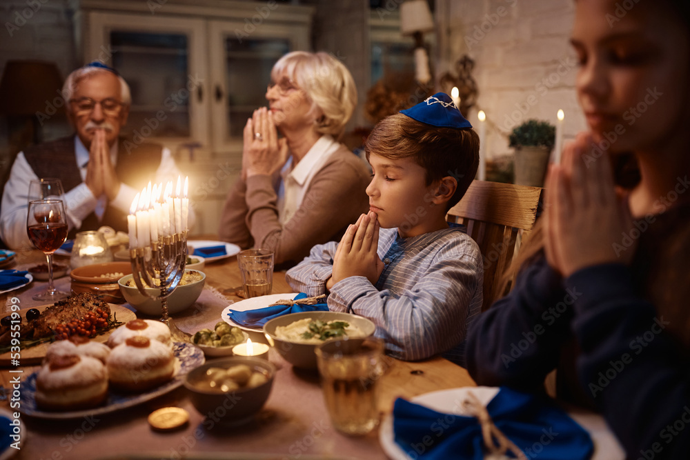 Jewish boy prays with his extended family at dining table on Hanukkah.