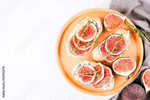 Fresh bruschettas with raw fig, cheese, prosciutto and herbs wooden plate with copy space on white background. Healthy on-the-go breakfast recipe. Top view, selective focus