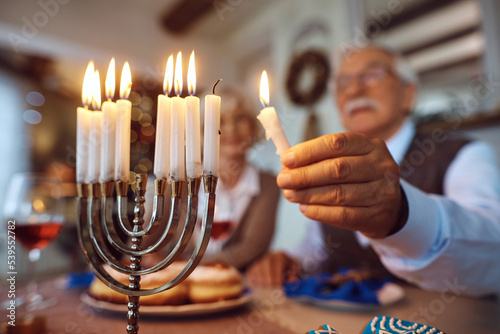 Close up of senior Jewish man lighting candle in menorah while celebrating Hanukkah with his wife. photo