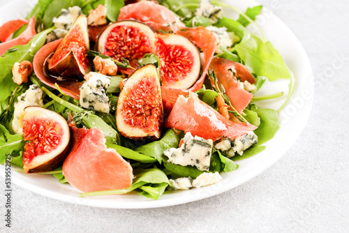 Healthy food recipe - salad with fresh fig, blue cheese, prosciutto, arugula and spinach on white table background with copy space. Lunch idea. Selective focus