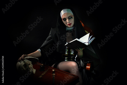 Принти на полотні An evil cursed nun with a notebook and a cross in her hands looks at the camera on a black background