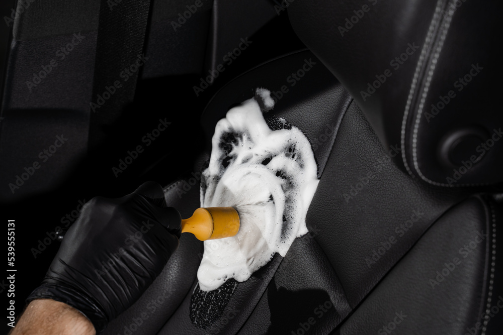 Process of foam and detergent cleaning leather seat using brush. Worker in auto cleaning service clean car inside. Car interior detailing. Process of foam and detergent cleaning leather seat using brush. Worker in auto cleaning service clean car inside. Car interior detailing.