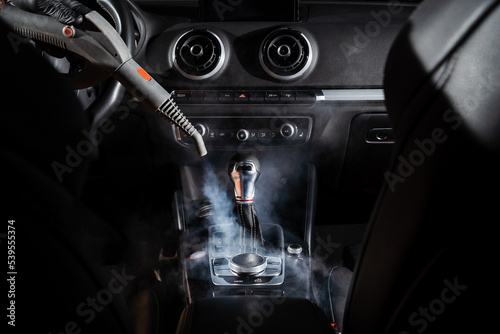 Steam cleaning of gearbox and dashboard in car. Vaping steam. Cleaning individual elements of black leather interior in auto. Creative advert for auto detailing service.