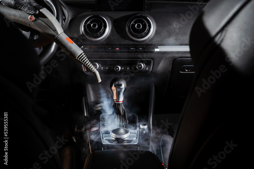 Steam cleaning of gearbox and dashboard in car. Vaping steam. Cleaning individual elements of black leather interior in auto. Creative advert for auto detailing service.