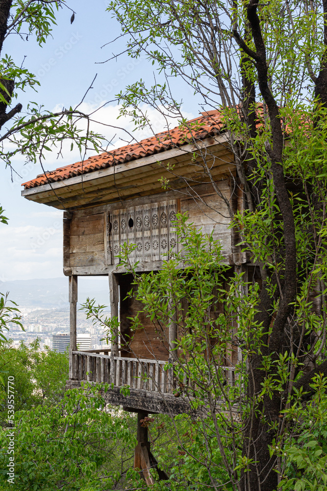 A traditional Georgian wooden farm building in Tbilisi Open Air Museum of Ethnography against the background of modern quarters of the capital. Georgia country A traditional Georgian wooden farm building in Tbilisi Open Air Museum of Ethnography against the background of modern quarters of the capital. Georgia country