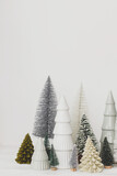 Stylish little Christmas trees on white background. Merry Christmas and Happy Holidays! Festive Christmas scene, miniature snowy forest. Modern minimal scandi decorations, holiday banne