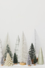 Merry Christmas and Happy Holidays! Stylish little Christmas trees on white background. Festive Christmas scene, miniature snowy forest. Modern minimal scandi decorations, holiday banner